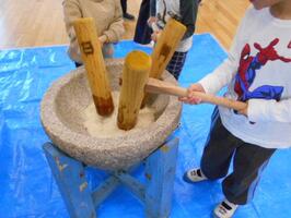 園児が三人で、小さな杵を持ち、餅をついています。