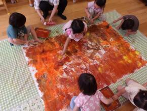 模造紙の上に道具を使って絵の具を塗り広げています。茶色や黄色が混ざり合い園庭で見つけた落ち葉のようです。