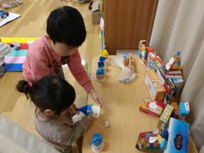 手作りおもちゃの的あてコーナーで、5歳児が1歳児に遊び方を伝えています。