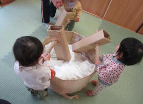 段ボールで作った杵と臼を使って、0歳児のこどもたちがもちつきごっこをしています。