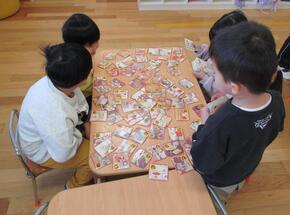 5人でテーブルを囲ってかるたをしています。並んだ絵札を見ているだけでも楽しくて会話が弾んでいます。