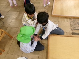 3歳児にコマの回し方を教える5歳児。4歳児もそばでみています。