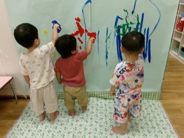 1歳児のこどもたちが筆で模造紙に絵を描いています。