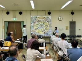 左に男子学生、中央に2メートル四方のパネル、右に女子学生が映った画像。パネルには学生が考えた泉北ニュータウンの未来像が描かれている。