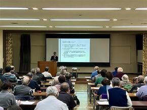 中央に資料を投影したスクリーン。左の演台にいる講師がマイクを持ち、和田文書について話している様子。